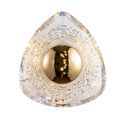 A modern geometric wall sconce featuring a clear faceted triangular crystal-like shade with a textured inner ring and a central gold metallic sphere, illuminated from within against a plain light background.