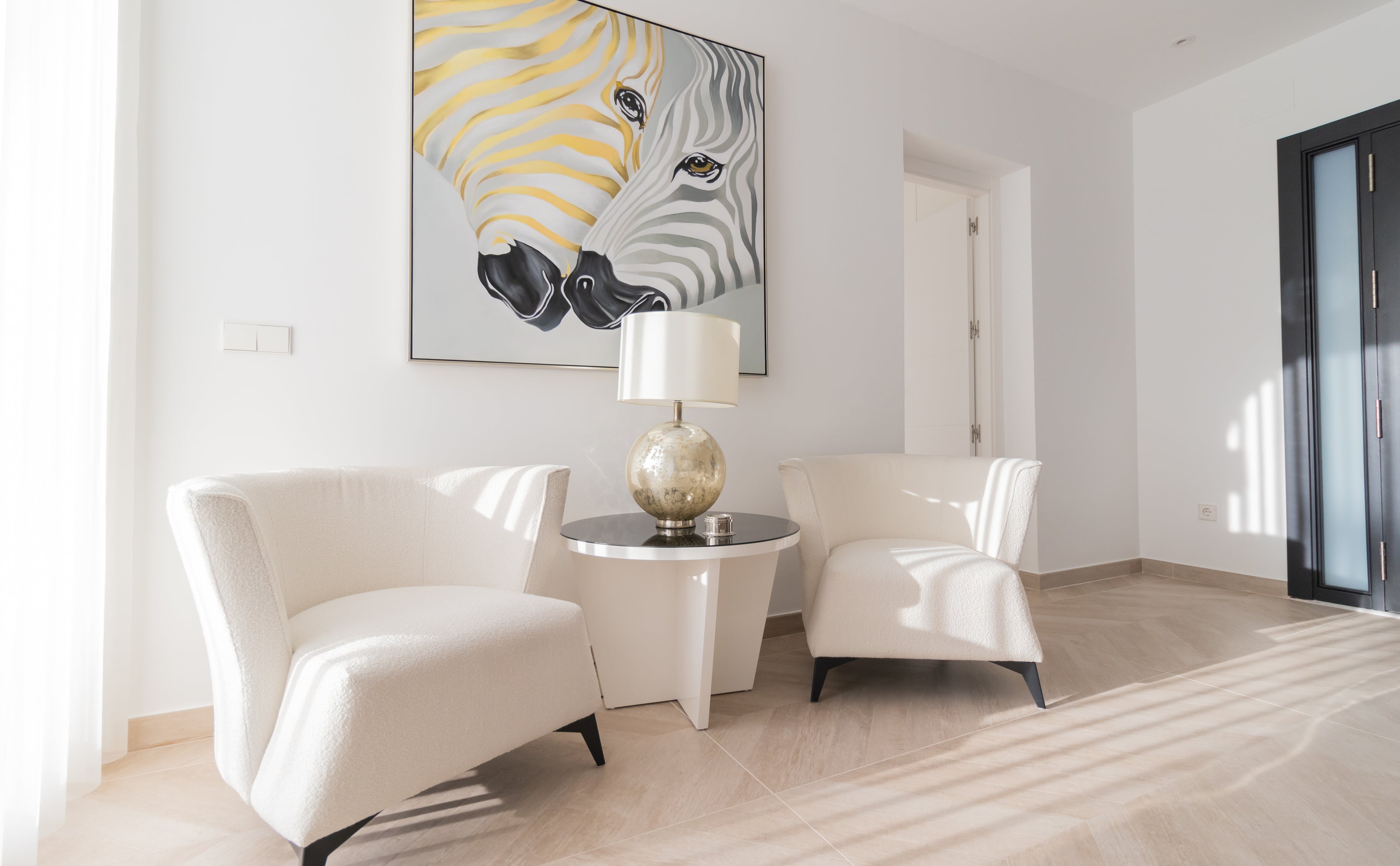 luxury interior design with 2 armchairs and modern side table, hanging zebra artwork with golden tones and table lamp available in el higueron, marbella, malaga, costa del sol.